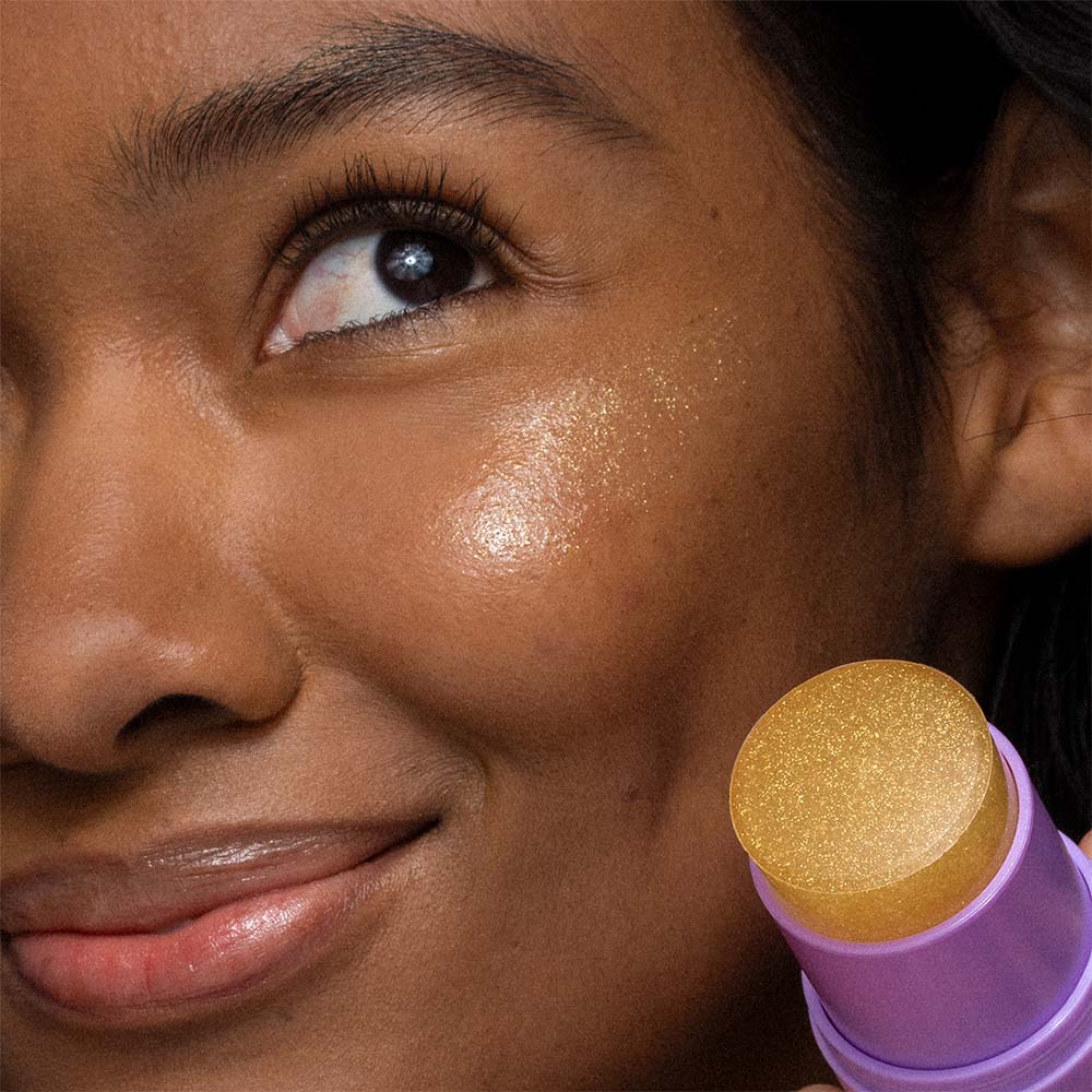 Eine Person trägt den Golden Hour Hydrating SPF 30 Stick auf ihre Wange auf und erzeugt dadurch einen nicht komedogenen, schimmernden, glasartigen Hautglanz.