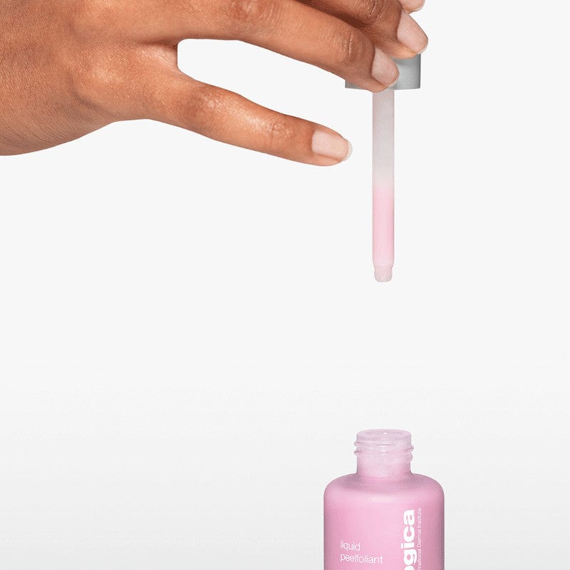 Hand hält einen Pipettentropfer über eine geöffnete Flasche mit rosa Flüssigkeit, beschriftet mit "liquid exfoliant".