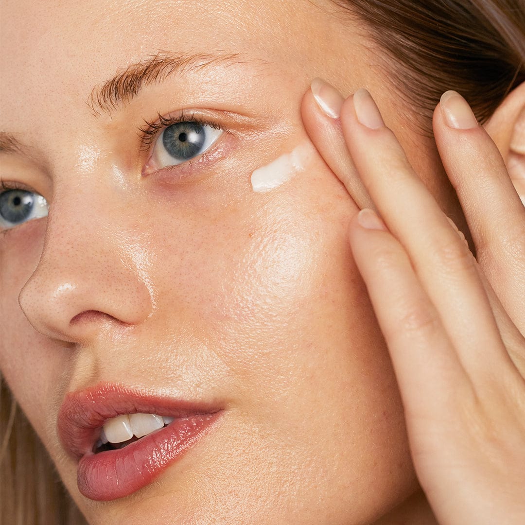 Nahaufnahme einer Frau, die Phyto Nature Lifting Eye Cream unter ihrem Auge aufträgt und so ihre klare Haut und ihre blauen Augen hervorhebt.