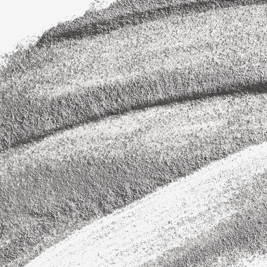 Nahaufnahme eines strukturierten grauen und weißen Pulvers, wahrscheinlich Daily Superfoliant mit Binchotan-Aktivkohle, das in geschwungenen, überlappenden Linien auf einer flachen Oberfläche angeordnet ist.