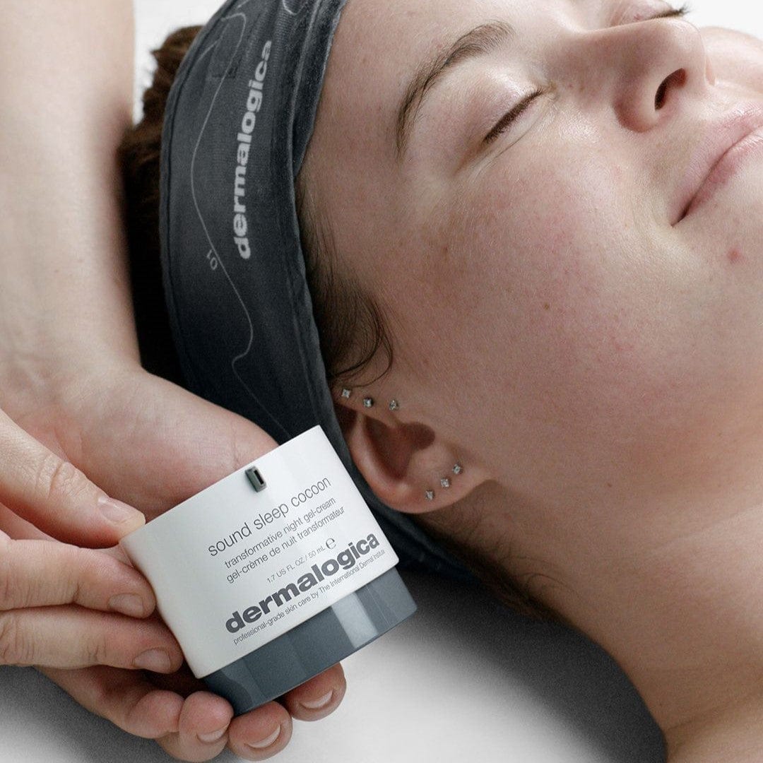 Eine Person mit Stirnband liegt mit geschlossenen Augen da und genießt den Aromatherapie-Effekt. Sie hält einen Behälter mit Sound Sleep Cocoon | Nachtpflege-Gelcreme neben ihr Gesicht und unterstützt so ihre transformative Nachtpflege und Hauterneuerungsprozesse.