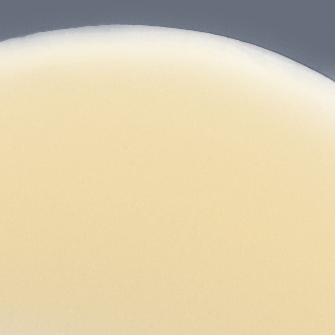 Nahaufnahme eines Bechers, der mit einer weißen, cremigen Flüssigkeit gefüllt ist, die an die Textur des Biolumin-C-Serums erinnert, mit dem oberen Rand des Bechers und einem neutralen Hintergrund.