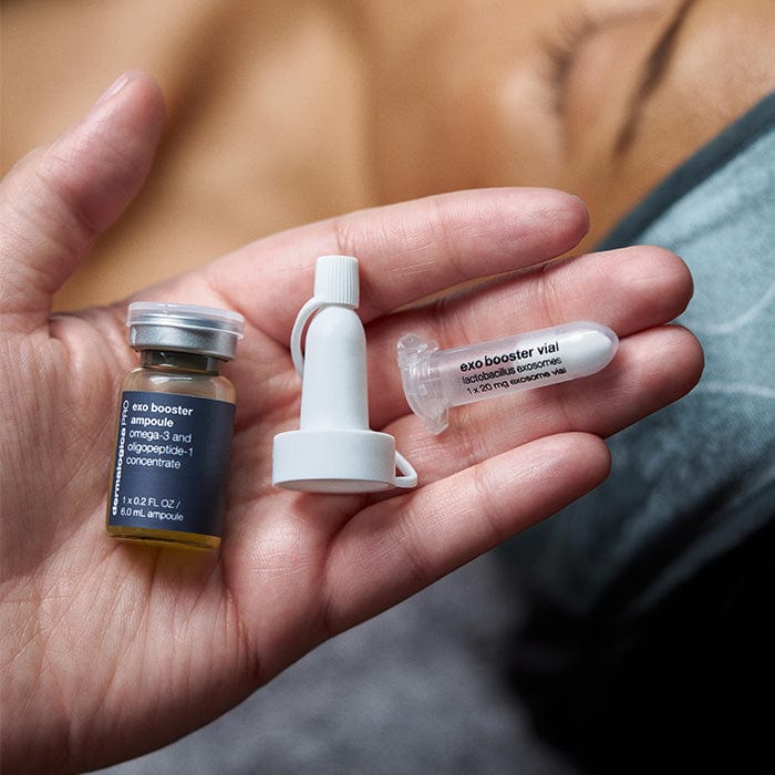 Eine Hand hält ExoBooster, ein kleines Fläschchen mit Lactobacillus-Exosomen, weißer Applikatorkappe und durchsichtigem Behälter - Teil eines topischen Boosters des Zwei-Phasen-Systems, der für die Anwendung von Microneedling entwickelt wurde.