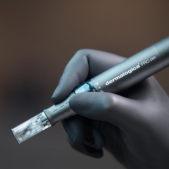 Eine behandschuhte Hand hält das Pro Pen Kit mit ExoBooster, ein professionelles Microneedling-Gerät mit klarer Spitze, vor einem unscharfen Hintergrund.