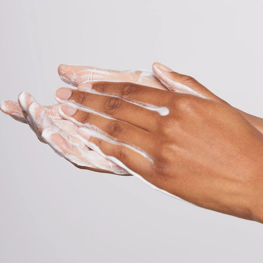 Die Hände einer Person tragen vor einem einfarbigen Hintergrund gründlich eine Joi Daily Microfoliant-Creme auf.