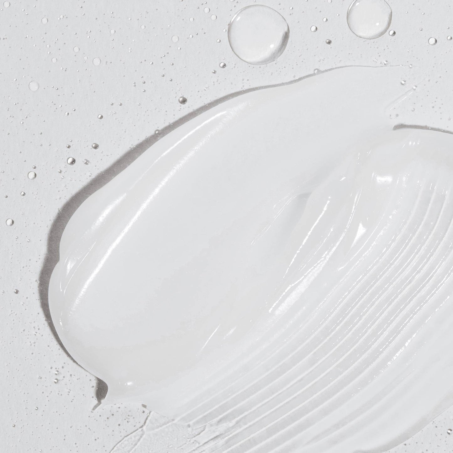 Eine Nahaufnahme der weißen Creme aus dem Sensitive Rescue Kit, die mit Wassertropfen auf eine strukturierte Oberfläche aufgetragen wurde – perfekt für empfindliche Haut und inspiriert von Dermalogica Produkten für ultimative Feuchtigkeit.