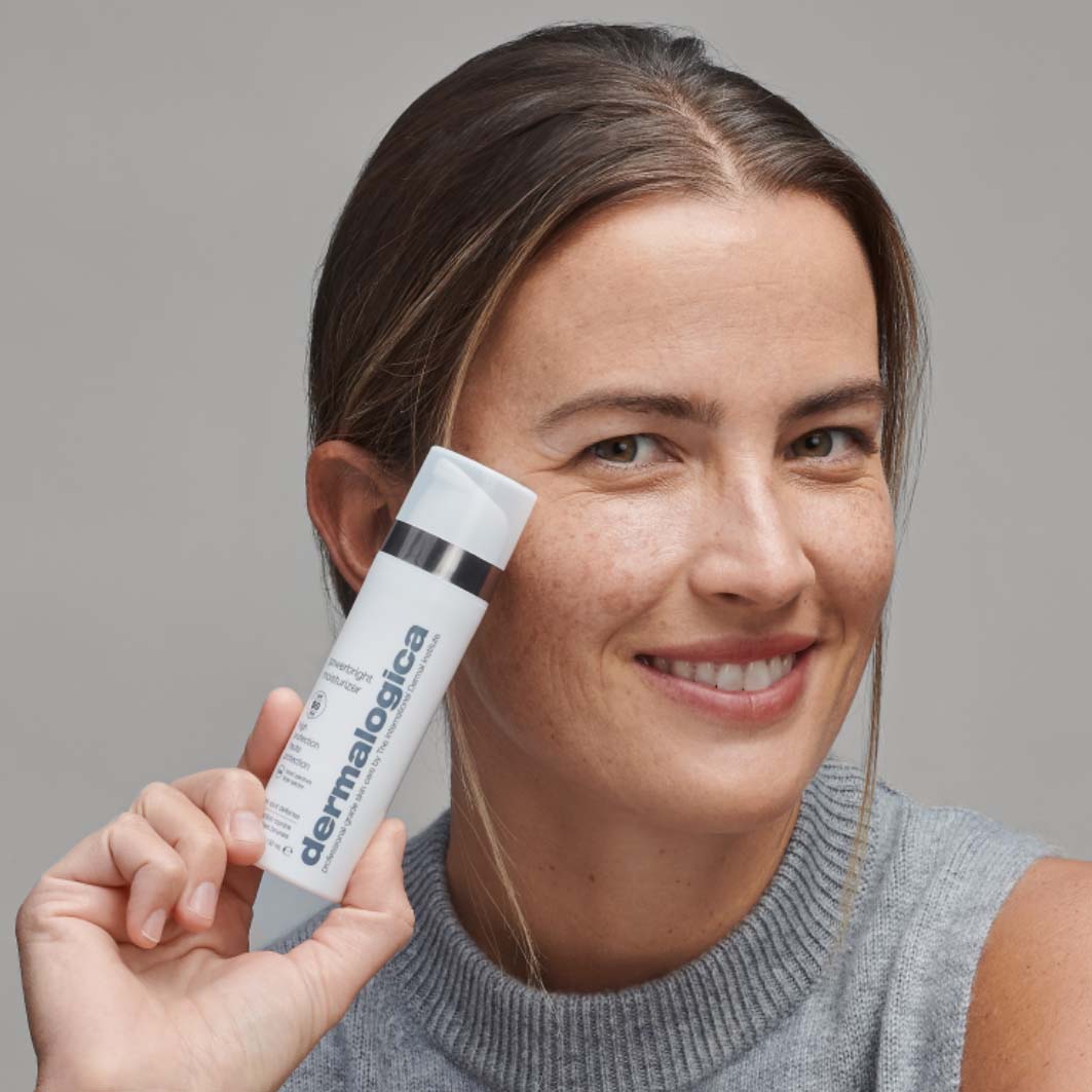 Lächelnde Person hält ein Produkt der Marke Dermalogica in der Hand.