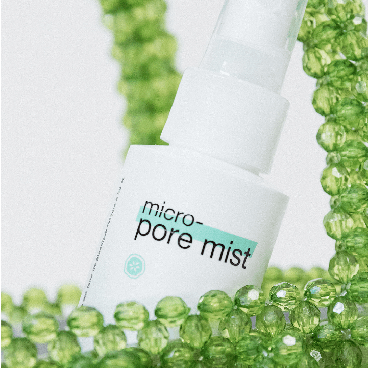 Flasche "micro pore mist" mit Sprühkopf vor einem Hintergrund aus grünen Perlen.