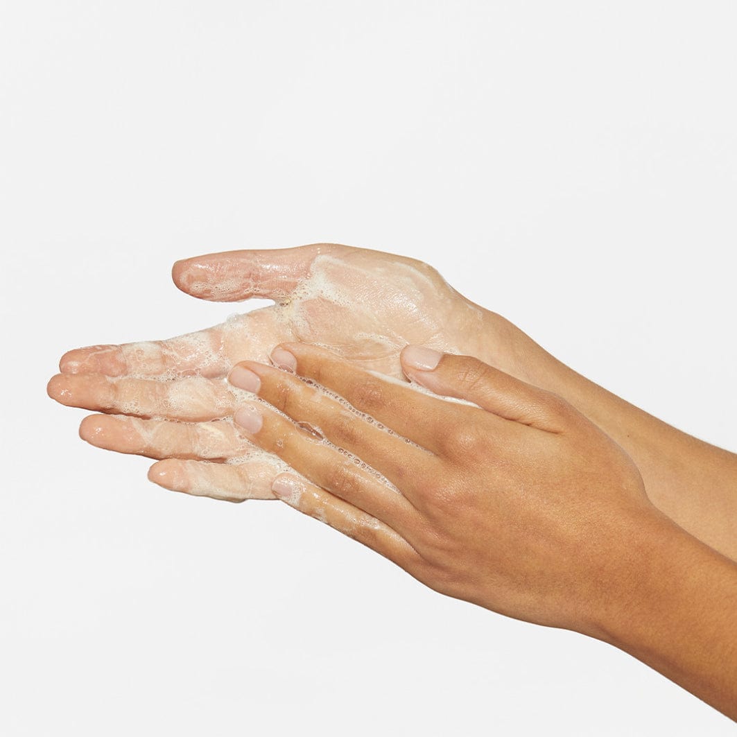 Hände mit aufgeschäumtem Hautpflegeprodukt auf weißem Hintergrund.