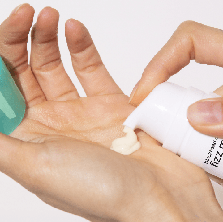 Eine Hand drückt eine Creme aus einer Tube auf die Fingerspitzen einer anderen Hand.