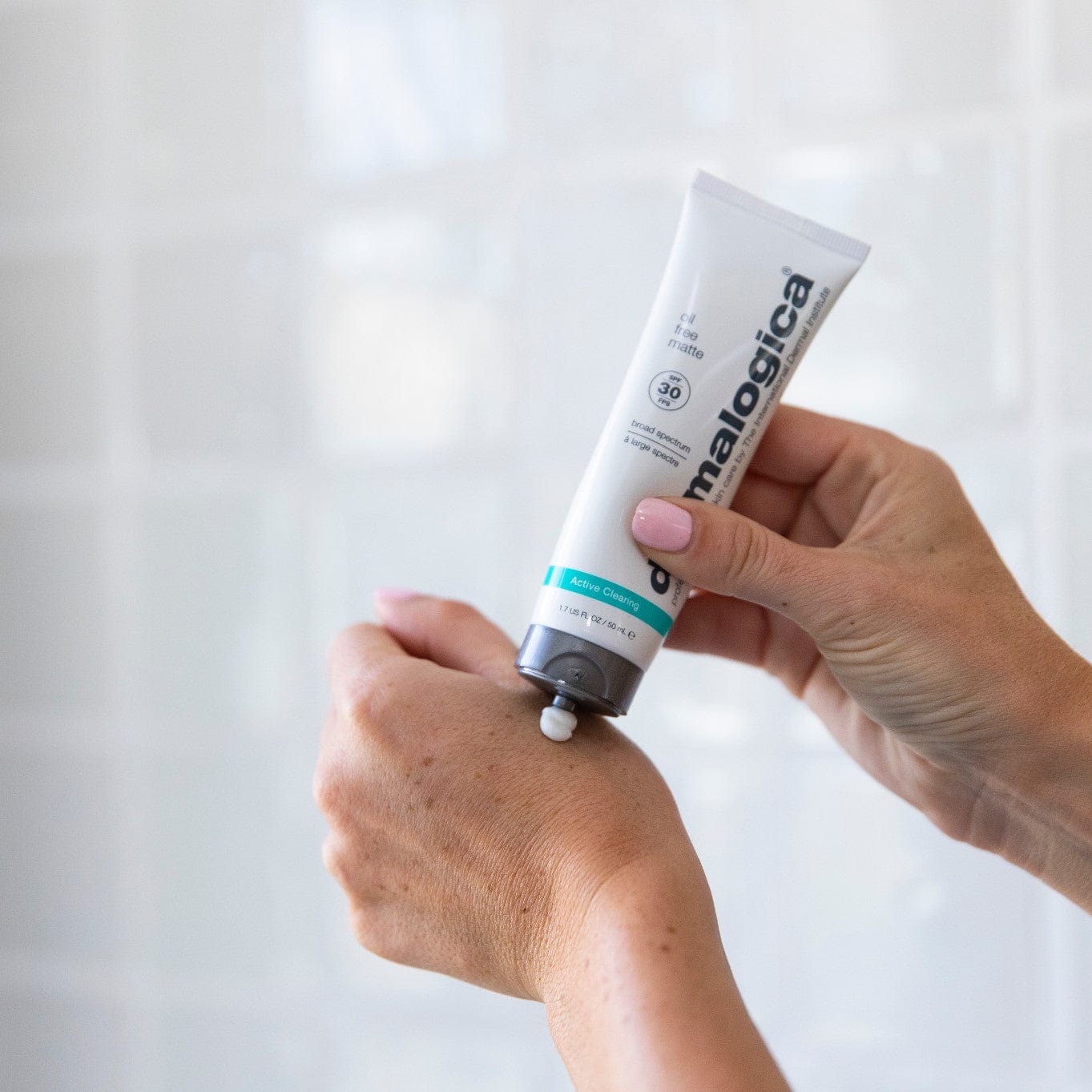 Person drückt eine Creme aus einer Tube der Marke Dermalogica auf den Handrücken.