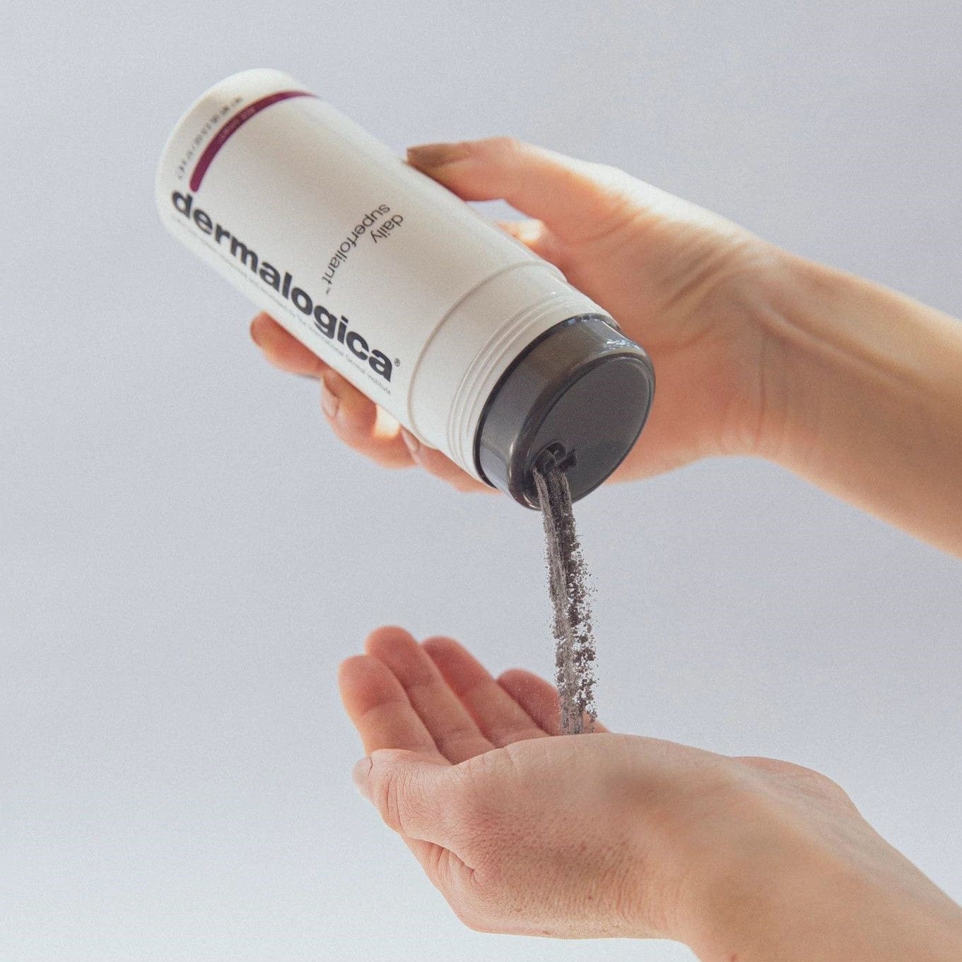 Eine Hand hält eine Dermalogica-Flasche und schüttet ein Pulverprodukt in die andere Handfläche.