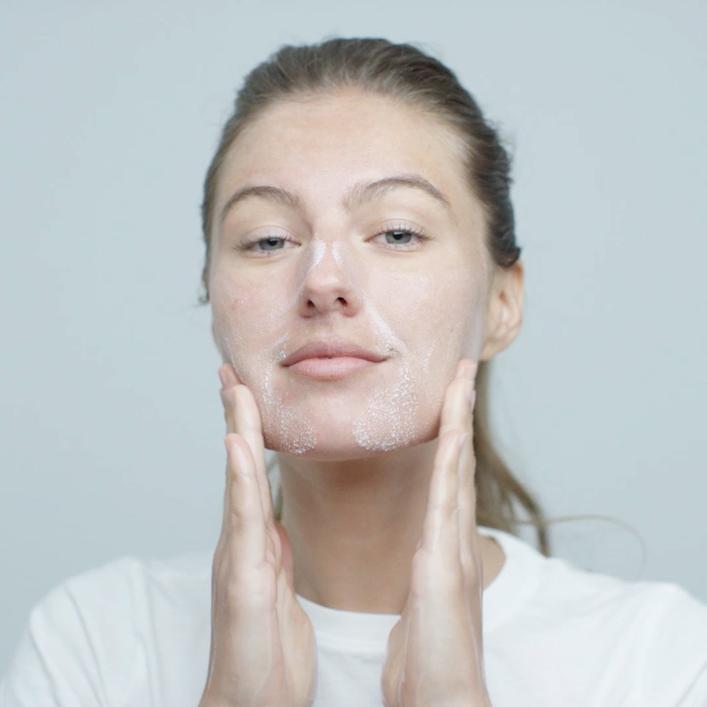 Frau mit aufgetragener Gesichtspflege, berührt sanft ihr Gesicht.