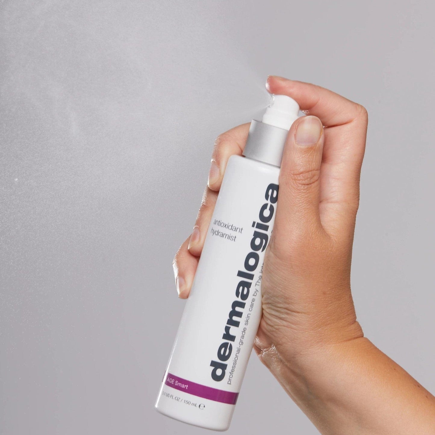 Eine Hand hält eine Flasche Dermalogica Antioxidant Hydramist gegen einen grauen Hintergrund.