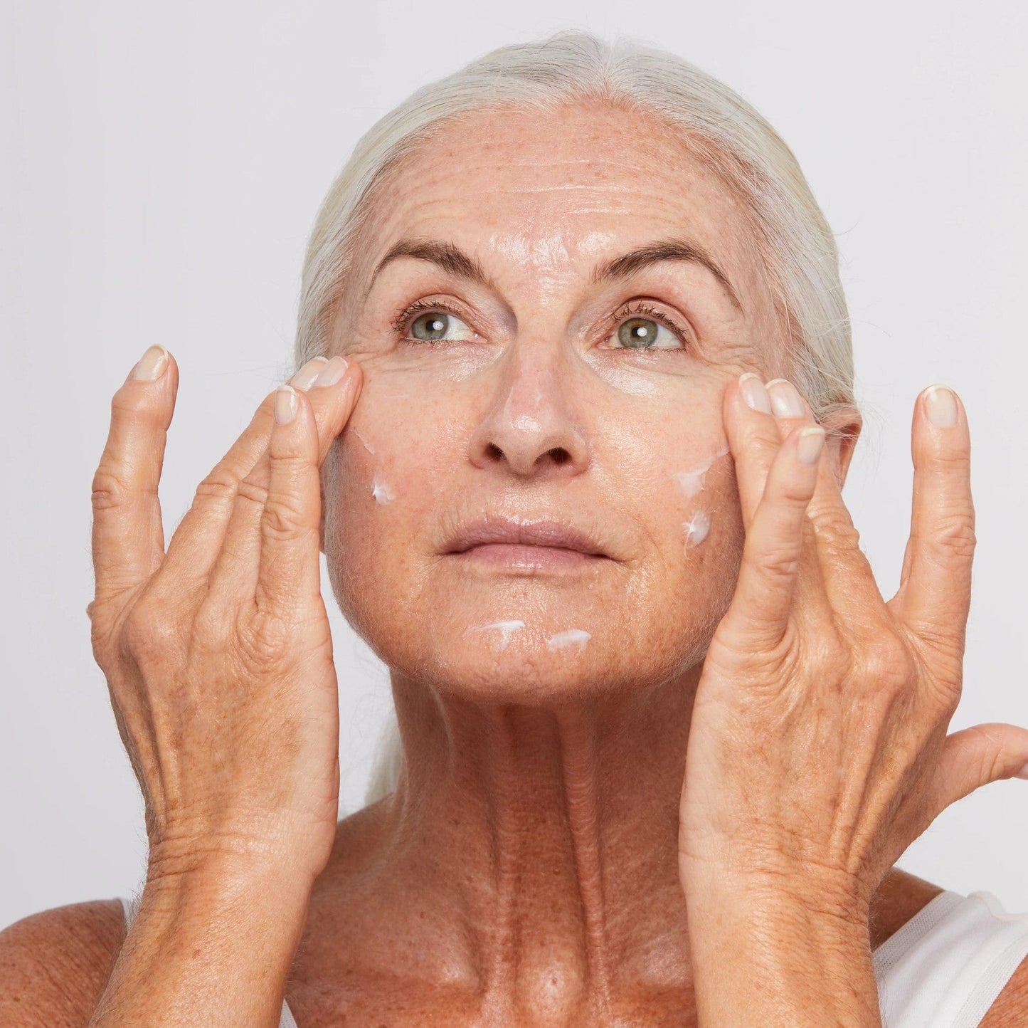 Ältere Frau trägt Gesichtscreme auf ihre Haut auf.