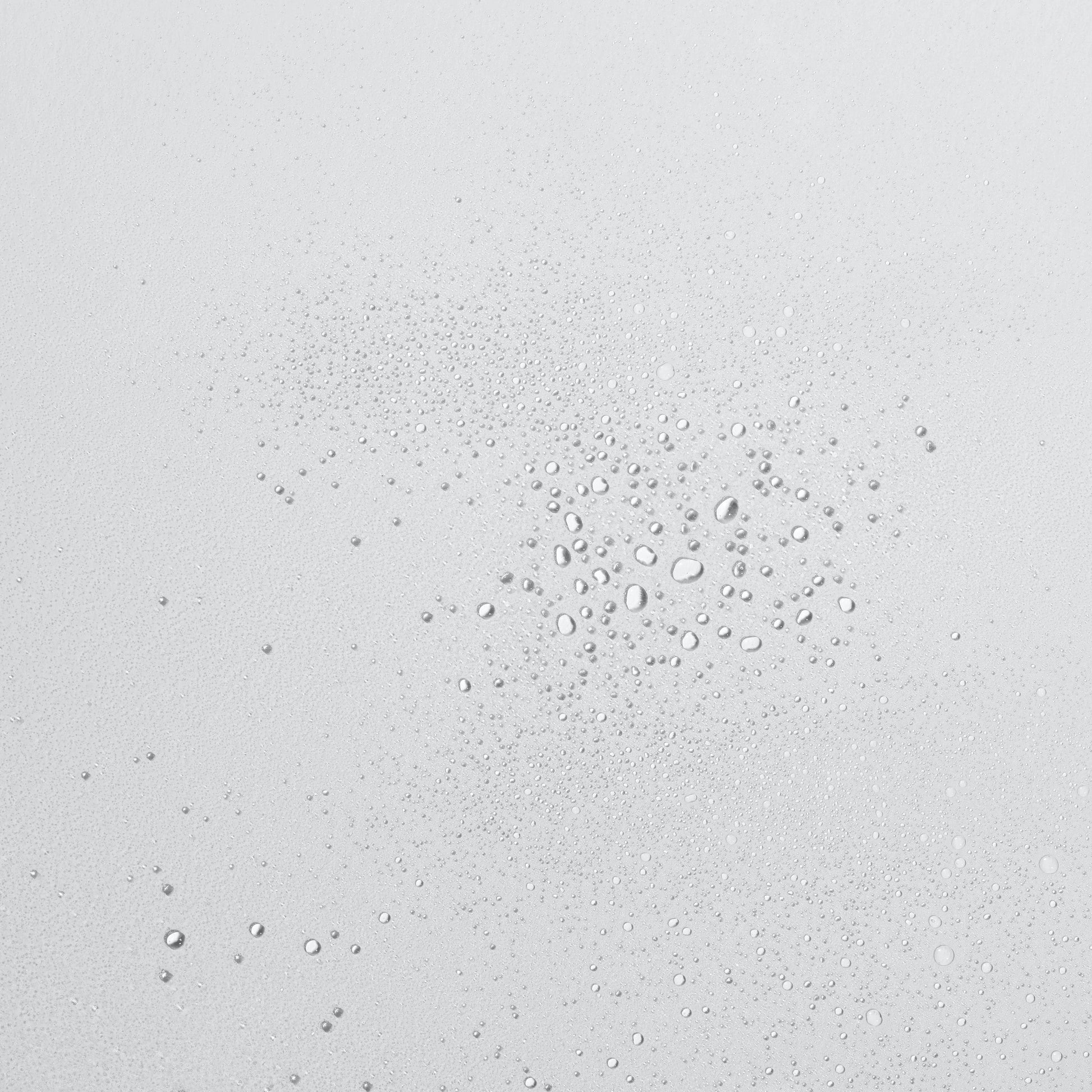 Tropfen klarer Flüssigkeit in verschiedenen Größen auf einer glatten, hellen Oberfläche.