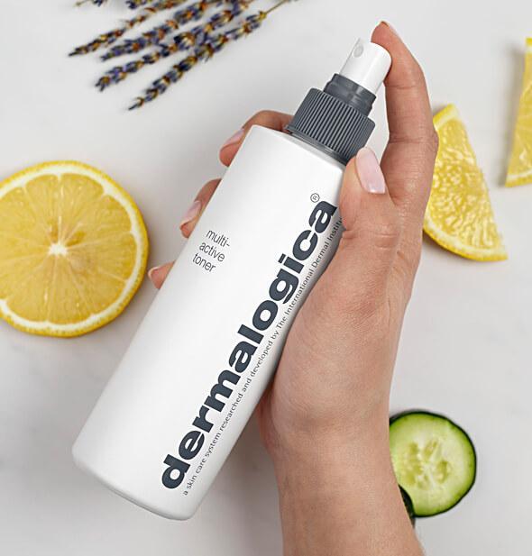 Eine Hand hält eine Flasche Dermalogica Multi-Active Toner neben Zitronenschnitzen und Gurkenscheiben auf einem hellen Hintergrund.