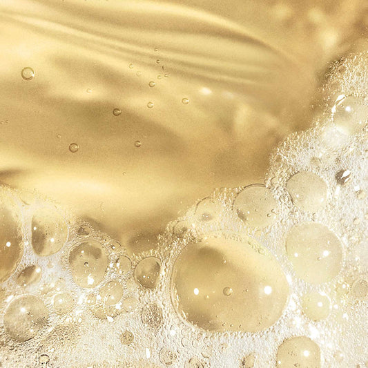 Nahaufnahme des hellgoldenen Oil To Foam Total Cleanser mit Schaum und Blasen auf der Oberfläche, die ein strukturiertes und glänzendes Erscheinungsbild erzeugen.