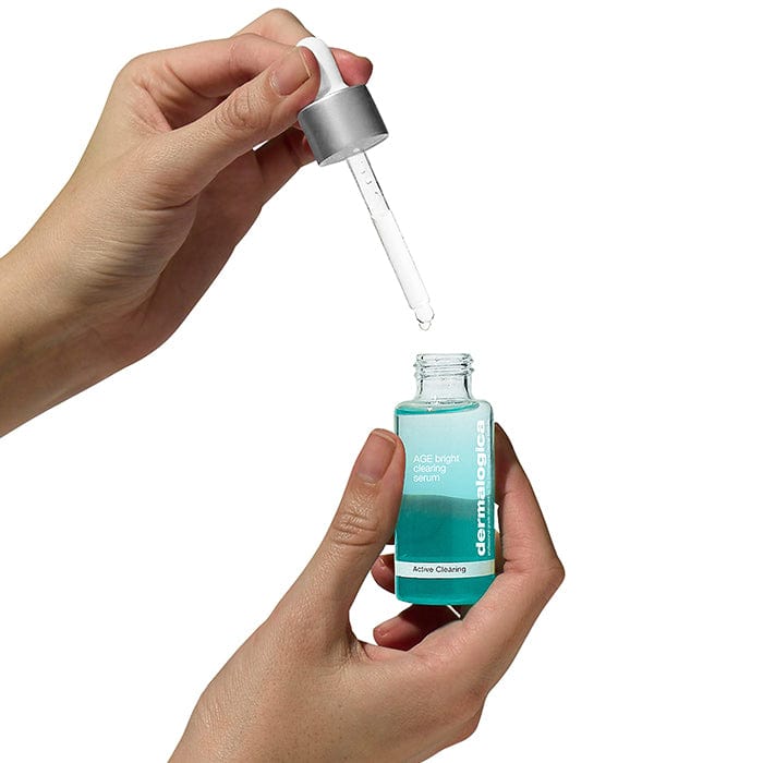 Eine Hand hält eine Flasche mit Flüssigkeit mit einer Pipette, die AGE Bright Clearing Serum 30 ml | enthält Pigmentausgleichendes Serum für Erwachsenenakne und Unreinheiten.