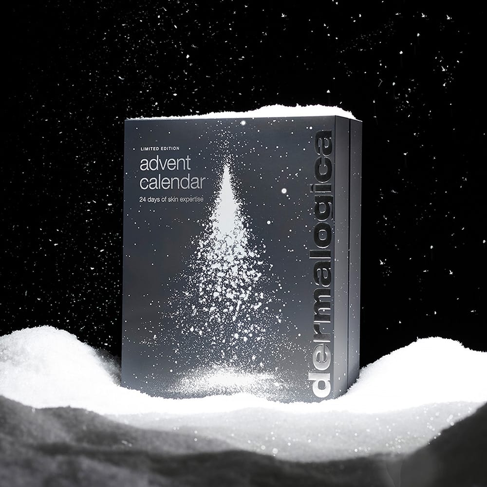 Eine graue Schachtel mit der Aufschrift „Adventskalender“ steht in Kunstschnee mit einem weißen Baummotiv. Der Dermalogica Premium-Adventskalender 2026 bietet 24 Tage lang Hautpflege-Überraschungen und trägt an der Seite den Markennamen „dermalogica“ – damit ist er das perfekte festliche Geschenk für jeden Hautpflege-Fan.