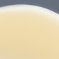 Nahaufnahme eines Bechers, der mit einer weißen, cremigen Flüssigkeit gefüllt ist, die an die Textur des Biolumin-C-Serums erinnert, mit dem oberen Rand des Bechers und einem neutralen Hintergrund.