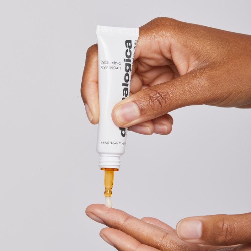 Vor einem schlichten Hintergrund gibt eine Hand Biolumin-C Augenserum aus einer Tube auf die Fingerspitze.
