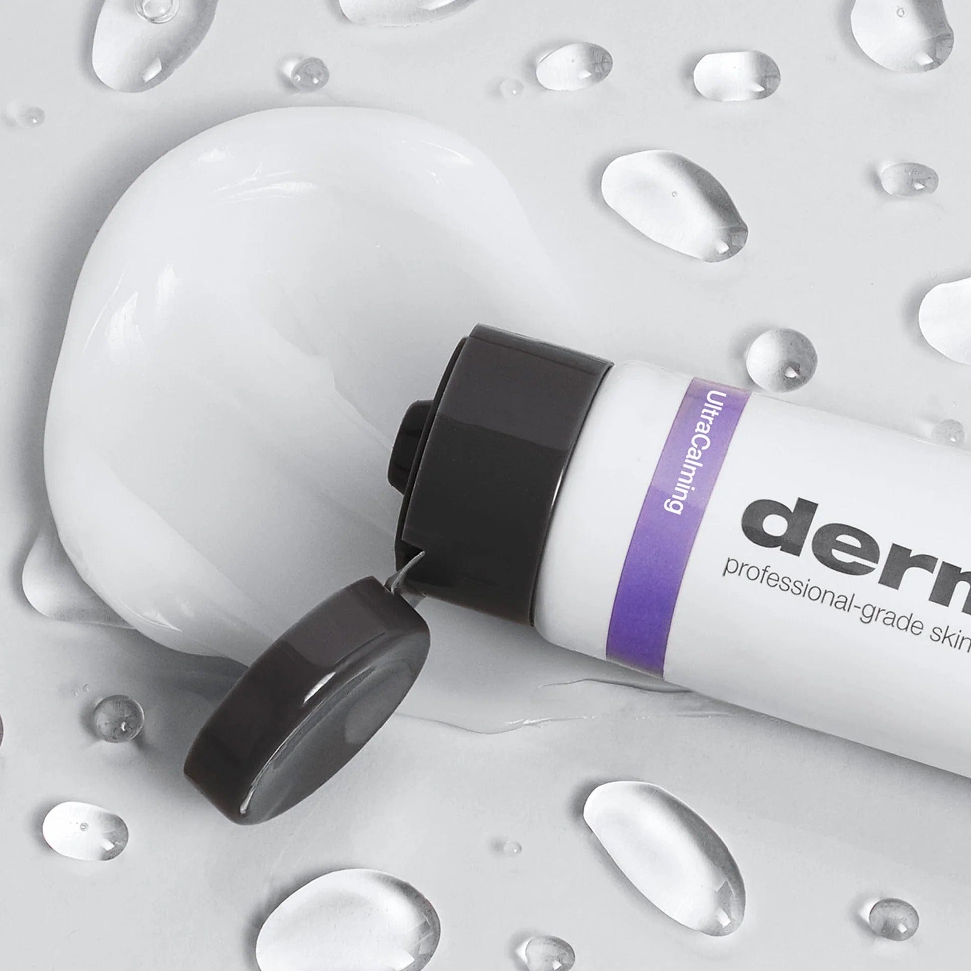 Eine Tube Calm Water Gel | Feuchtigkeitspflege mit geöffnetem schwarzen Klappdeckel, umgeben von Geltropfen auf einer hellen Oberfläche, enthält den UltraCalming-Komplex zur Beruhigung und zum Schutz empfindlicher Haut.