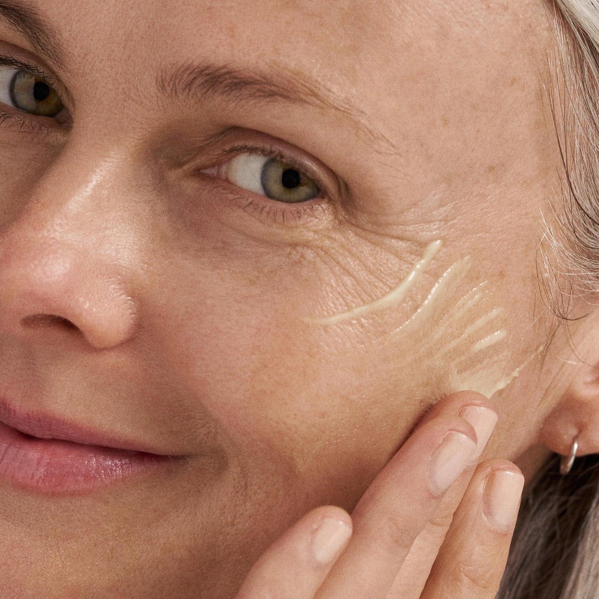 Nahaufnahme einer Frau, die das Dynamic Skin Retinol Serum mit den Fingern auf ihre Wange aufträgt, um sichtbare Falten und die natürliche Hautstruktur zu betonen.