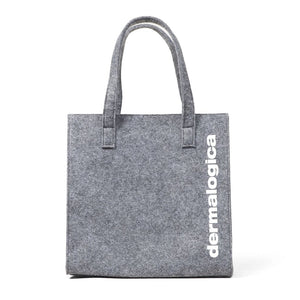 Die Dermalogica Tote Bag gratis ist eine graue Filztasche mit zwei Henkeln, dem Aufdruck "dermalogica" senkrecht in weiß auf der rechten Seite, einer einfachen rechteckigen Form und der Kennzeichnung "kein Verkaufsprodukt" (not for resale).