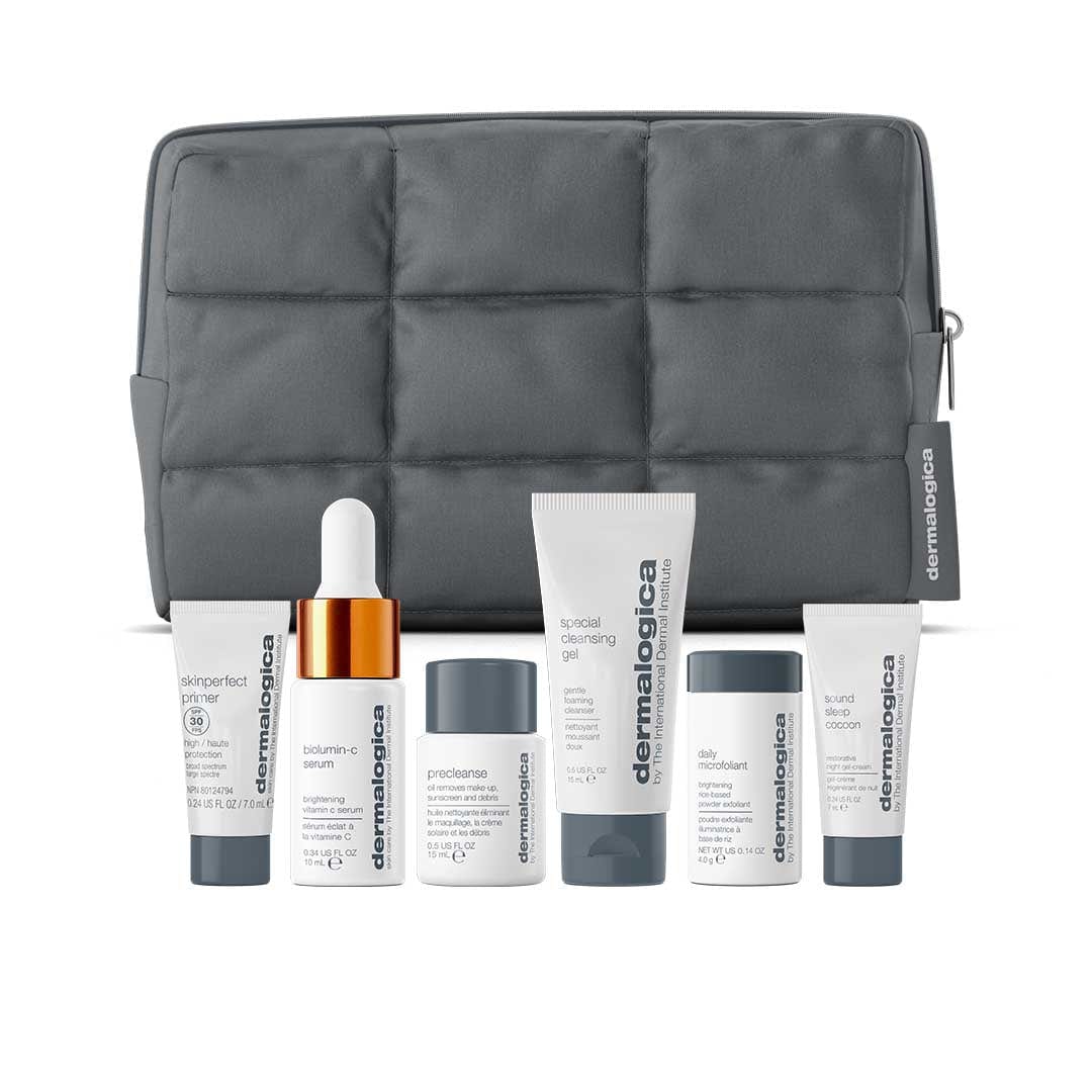 Eine graue, gesteppte Kosmetiktasche aus dem Set "6 Minis + Tasche im Wert von 133€" steht hinter sieben Dermalogica Minis in Reisegröße, die fein säuberlich in einer Reihe angeordnet sind.