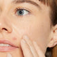 Nahaufnahme eines Gesichtsbereiches mit Augenpartie und Wange einer Person, die ihre Haut berührt.