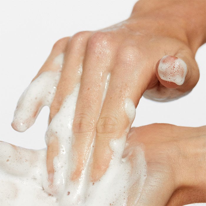 Eine Person, die den Oil To Foam Total Cleanser verwendet, um ihre Hände mit Seife zu waschen.