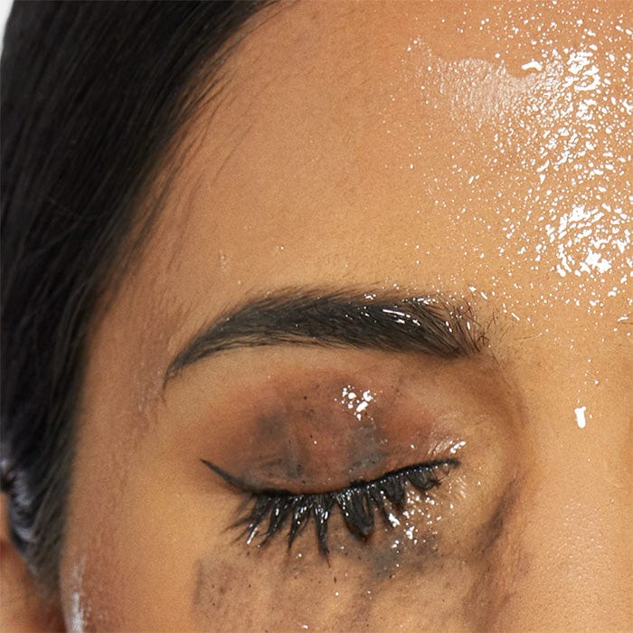 Nahaufnahme eines geschlossenen Auges mit Mascara, Eyeliner und glänzenden Partikeln auf der Haut.