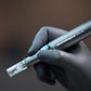 Eine behandschuhte Hand hält das Pro Pen Kit mit ExoBooster, ein professionelles Microneedling-Gerät mit klarer Spitze, vor einem unscharfen Hintergrund.