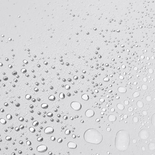 Wassertropfen unterschiedlicher Größe, die über eine glatte, hellgraue Oberfläche verstreut sind, erinnern an die erfrischende Note von Antioxidant HydraMist.