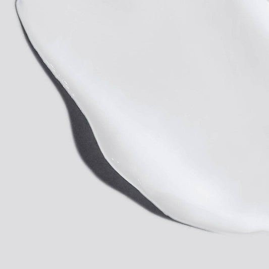 Eine Nahaufnahme der Body Hydrating Cream, einer weißen Flüssigkeit, die auf einer glatten, hellgrauen Oberfläche verteilt ist – ideal, um luxuriöse vegane Hautpflege hervorzuheben.