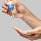 Eine Hand hält eine Pipettenflasche über eine andere Handfläche und lässt einen Tropfen Flüssigkeit fallen.