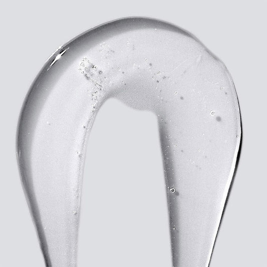 Ein klares, dickflüssiges Gel des Conditioning Body Wash mit Provitamin B5 wird bogenförmig auf einen schlichten grauen Untergrund aufgetragen; in der pflegenden Formel sind kleine Luftbläschen sichtbar.