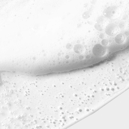 Nahaufnahme eines weißen Schaums mit Bläschen auf einer glatten weißen Oberfläche, der die mit pflegendem Jojoba-Samenöl angereicherte Daily Glycolic Cleanser enthält.