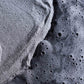 Nahaufnahme des feinen grauen Daily Superfoliant-Puders, der mit einer dunklen, sprudelnden Flüssigkeit verschmilzt, was auf eine erhöhte Kollagenproduktion ohne Risiko von Hautschäden hindeutet.