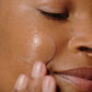 Eine Person trägt Liquid Peelfoliant mit den Fingern auf ihre Wange auf, wodurch glatte, hydratisierte Haut und sichtbar reduzierte feine Linien zum Vorschein kommen.