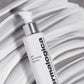 Eine Flasche Skin Resurfacing Cleanser steht auf einer strukturierten Oberfläche, die seidige Formel ist darauf verteilt.