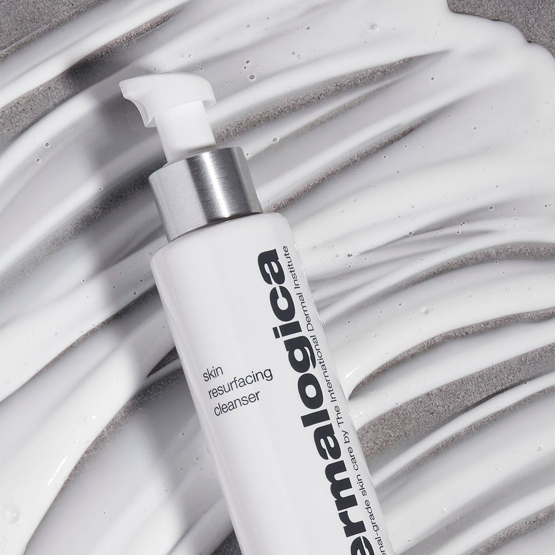 Eine Flasche Skin Resurfacing Cleanser steht auf einer strukturierten Oberfläche, die seidige Formel ist darauf verteilt.