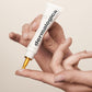 Eine Hand hält eine Tube Dermalogica Biolumin-C Serum mit einer Tropfenspitze, aus der ein Tropfen auf den Finger der anderen Hand fällt.