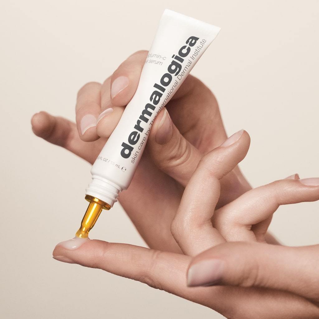 Eine Hand hält eine Tube Dermalogica Biolumin-C Serum mit einer Tropfenspitze, aus der ein Tropfen auf den Finger der anderen Hand fällt.