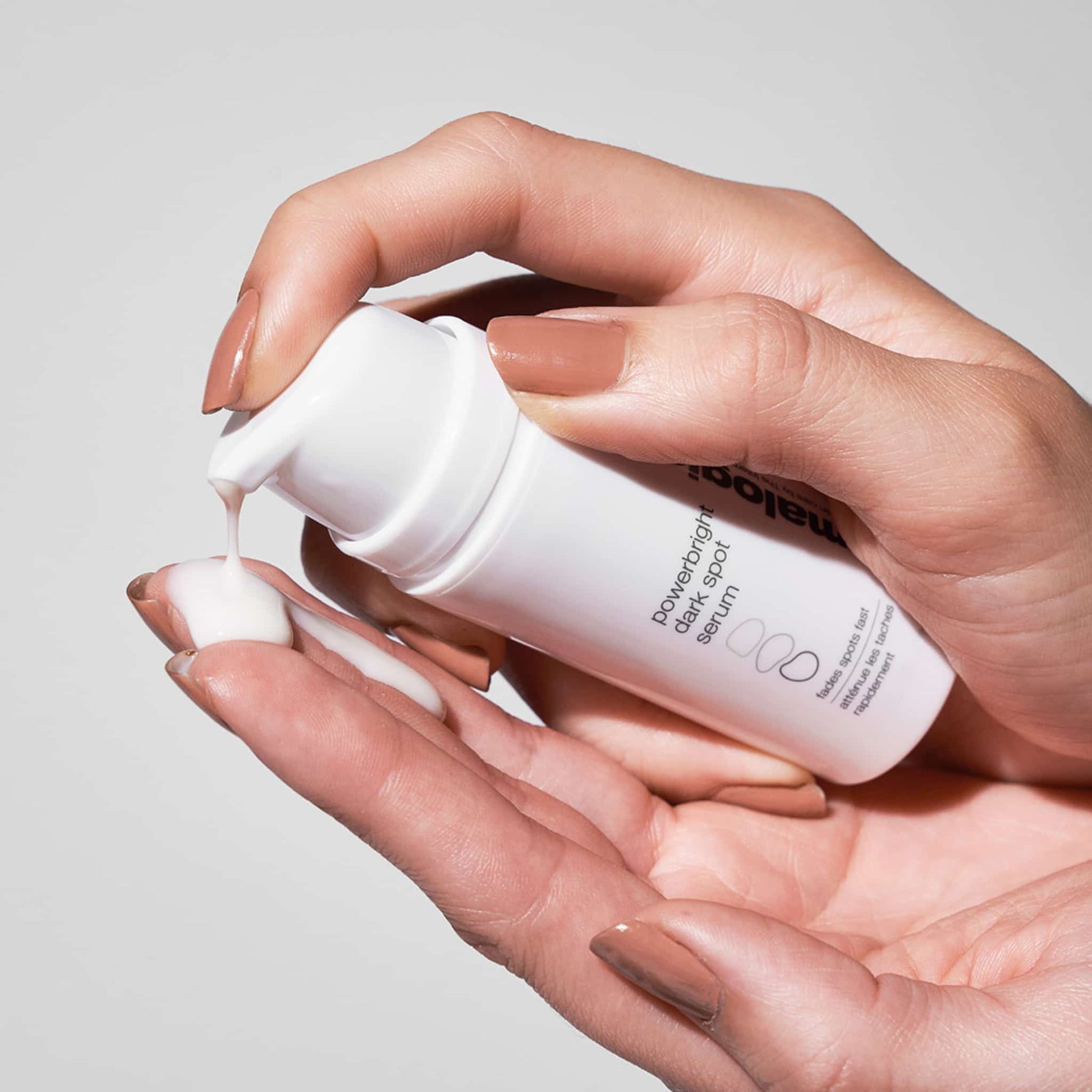 Hände drücken eine Lotion oder ein Serum aus einer weißen Flasche in die Handfläche.