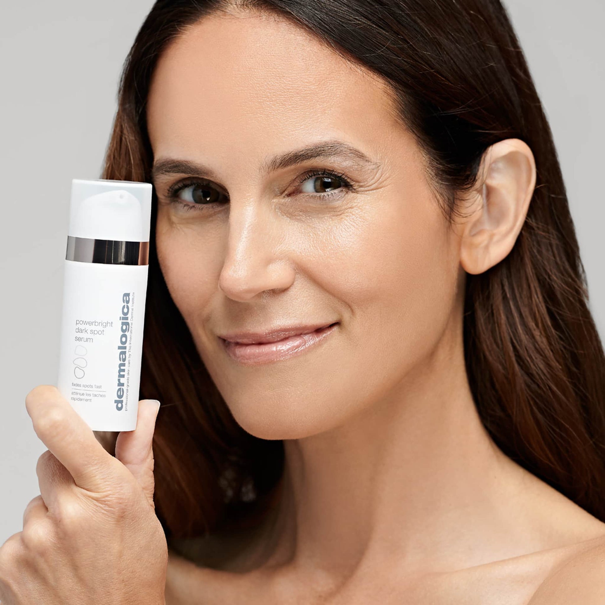 Lächelnde Frau hält eine Flasche Powerbright Dark Spot Serum in der Hand.