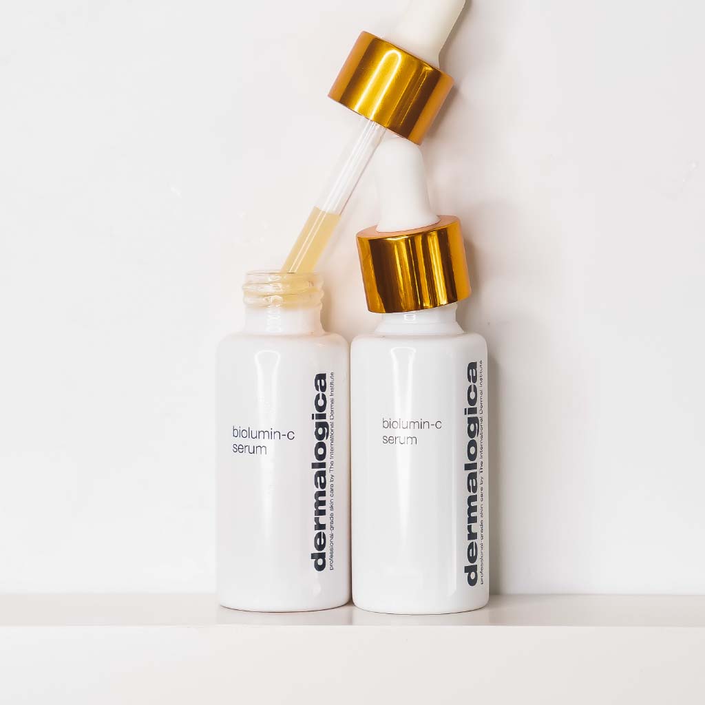 Zwei weiße Flaschen von BioLumin-C Serum auf einem hellen Hintergrund, eine mit geöffnetem Deckel und sichtbarem Tropfer