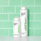 Zwei Flaschen ' Breakout Clearing Foaming Wash' stehen vor einer Wand mit grünen Fliesen.
