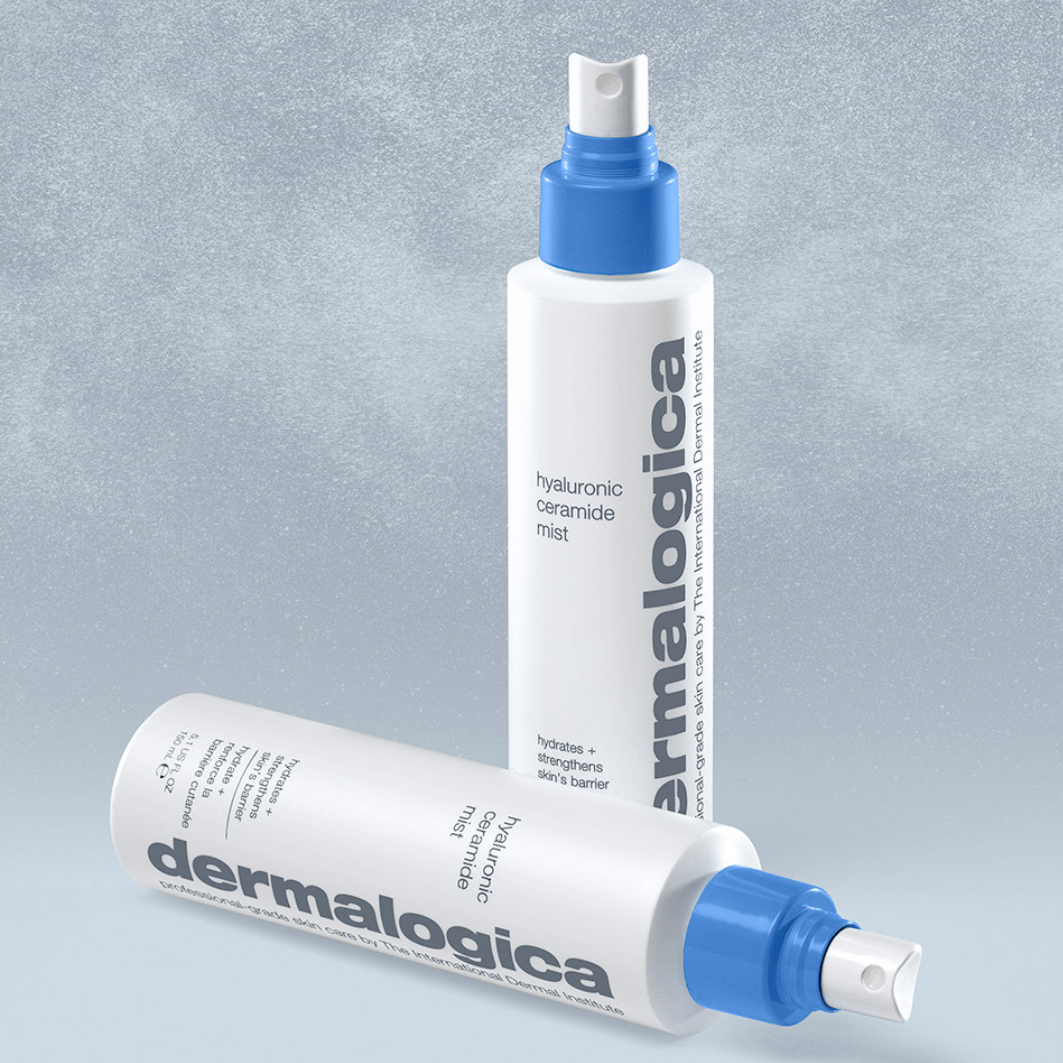 Dermalogica Hyaluronic Ceramide Mist Flasche im hinteren Bereich aufrecht stehend und eine zweite liegend im Vordergrund auf texturierter grauer Oberfläche.